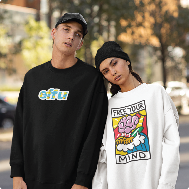 A man and woman stand side by side outdoors, both wearing sweatshirts. The mans is black with colorful text, and the womans is white with a graphic and the words Free Your Mind.