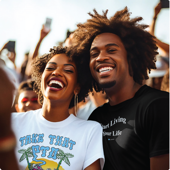 A smiling couple enjoys a concert in a crowd, with the sun illuminating their joyful faces. The woman wears a Take That Trip shirt, and the man wears a Start Living Your Life shirt.