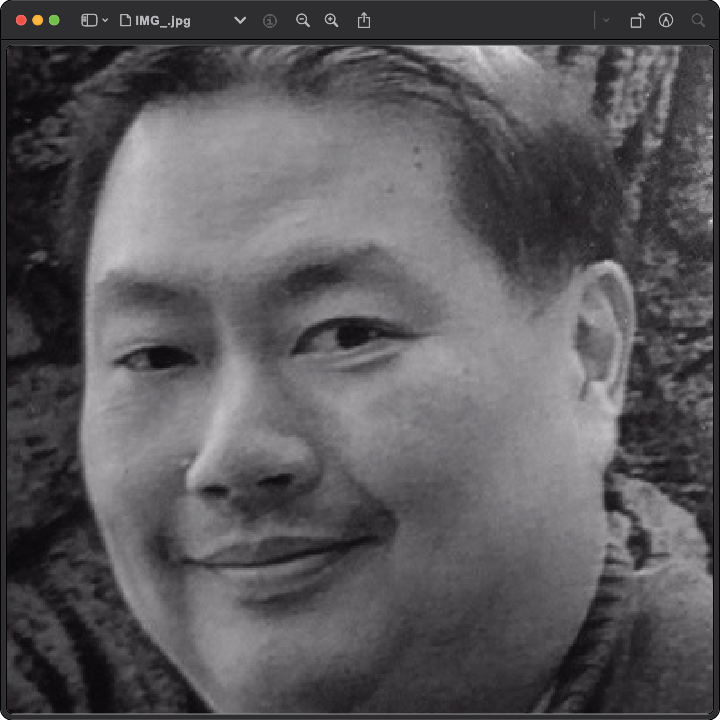 A close-up black and white photograph of a smiling man with short hair in a natural setting.