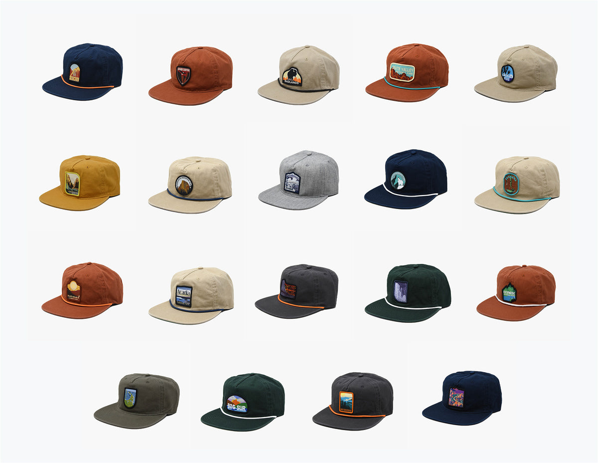 A grid of 21 colorful baseball caps, each featuring unique embroidered patches with various designs and colors on their front panels.